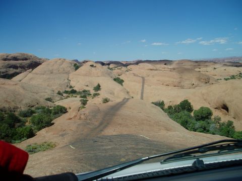 2000 Ford E350 - Driver's-eye view over the dashboard, cowl vent and wiper of a vehicle cresting a steep red slickrock fin, with the trail's tire-worn track…