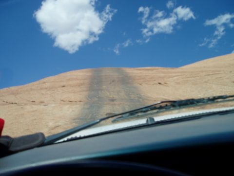 2000 Ford E350 - Driver's-eye view over the dash and windshield wipers while climbing a steep slickrock dome under a deep blue sky. Only the dark dashboard…