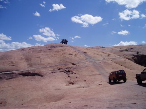 2000 Ford E350 - Multiple off-road vehicles navigate a challenging rocky terrain under a bright, cloudy sky.