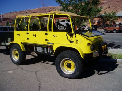 2000 Ford E350 - This bright yellow Unimog, likely used for off-road tours, is parked on a street with a desert landscape in the background.