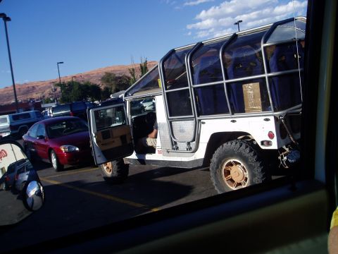 2000 Ford E350 - A white, modified Humvee with a custom cage and seating is parked in a lot with other vehicles.