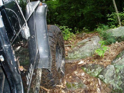 2000 Ford E350 - A Jeep navigates a rocky, off-road path in a wooded area.