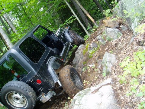 2000 Ford E350 - A black Jeep Wrangler navigates a challenging rocky trail in a wooded area.