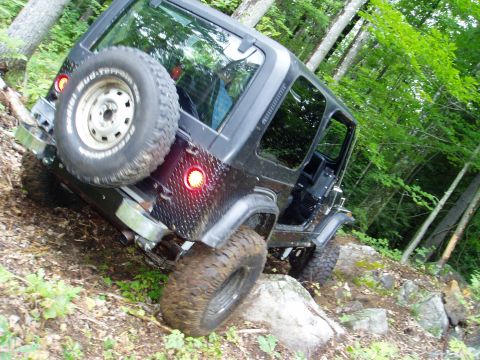 2000 Ford E350 - A Jeep Wrangler TJ navigates a challenging, rocky incline surrounded by dense forest foliage.