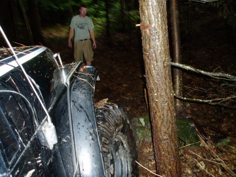 2000 Ford E350 - A black van is stuck off-road, with a person standing behind it and trees surrounding it.