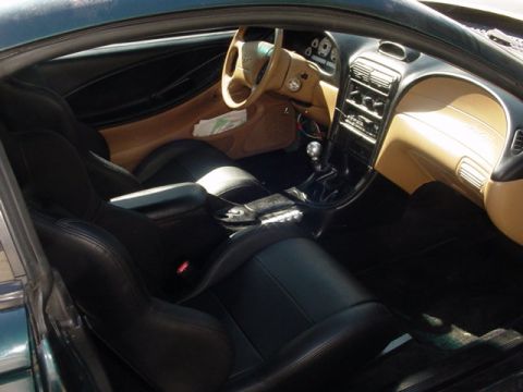1995 Ford Mustang - Interior view of a car with black leather seats and a tan dashboard, showing the steering wheel and center console.