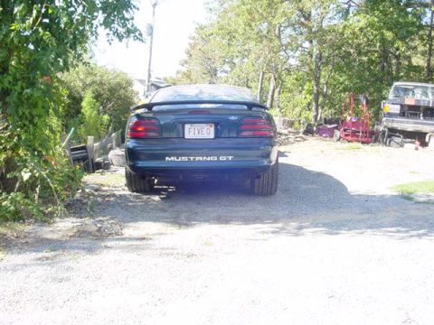 1995 Ford Mustang - A 1995 Ford Mustang GT is parked in a gravel lot with trees and another vehicle visible in the background.