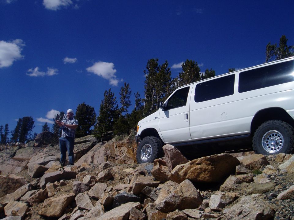 White 2000 Ford E350 van with off-road tires on rocky slope