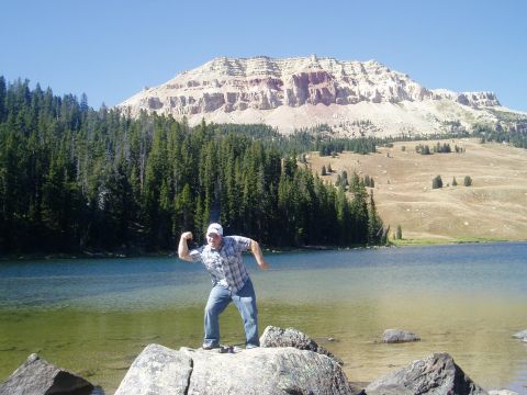 2000 Ford E350 - A man poses by a clear lake with a mountain range and pine forest behind him.