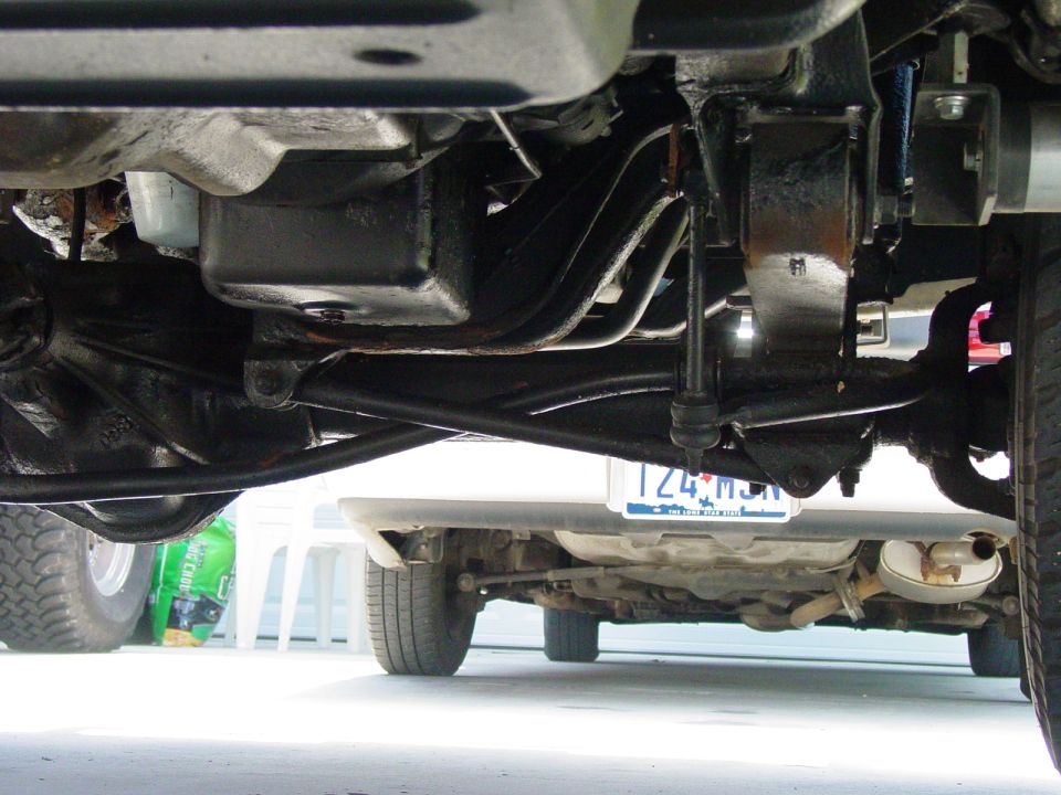 Underside of a truck, showing suspension and exhaust. Another car is visible underneath