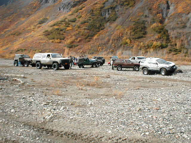 Row of lifted 4x4 trucks and Jeeps parked on a gravel riverbar below autumn mountainside