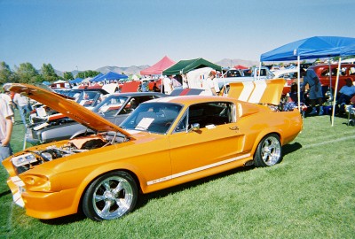 1972 Ford Ranchero - An orange muscle car with white racing stripes is displayed at an outdoor car show with its hood and trunk open.
