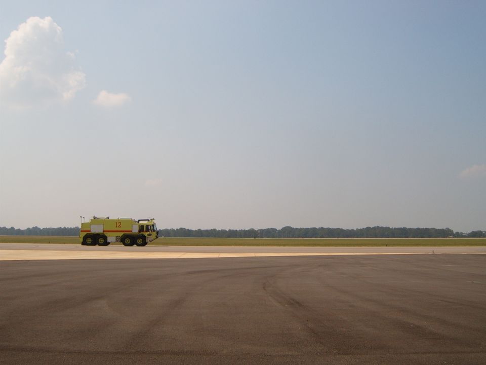 Yellow airport fire truck with number 12 on side, driving on tarmac