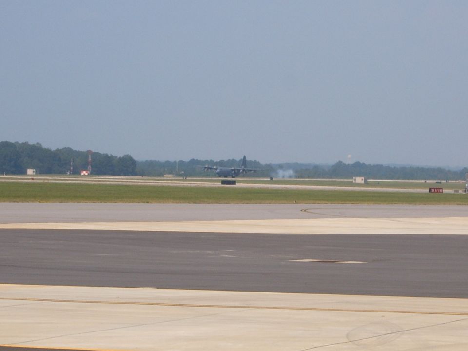 Military transport aircraft on an airport runway, with smoke trailing