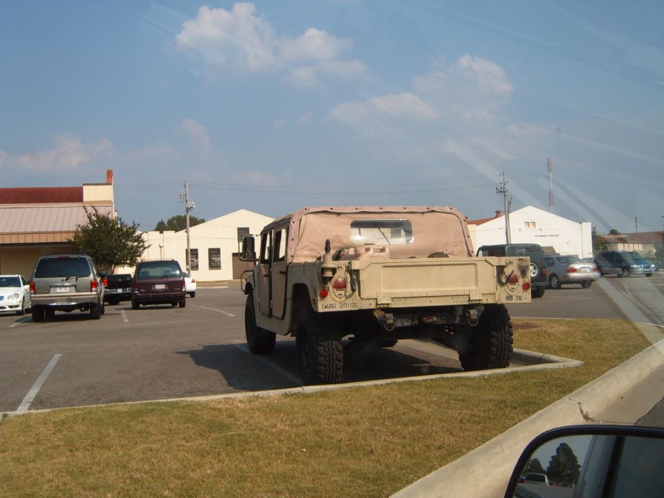 Tan military vehicle with a soft top, parked in a lot. Visible text on rear