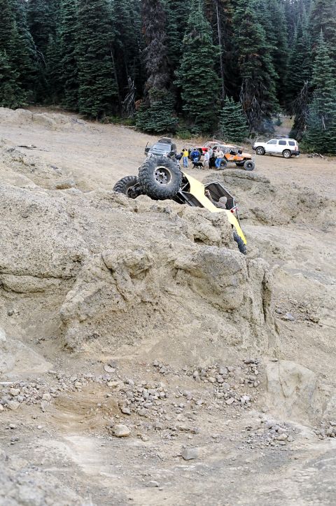 1979 Ford Bronco - An off-road buggy has tipped over on a steep, rocky incline while onlookers observe the scene.