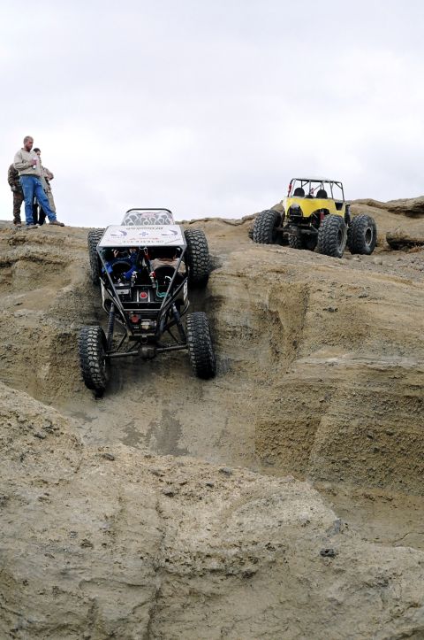 1979 Ford Bronco - Two heavily modified off-road vehicles tackle a challenging rocky ascent with spectators observing.