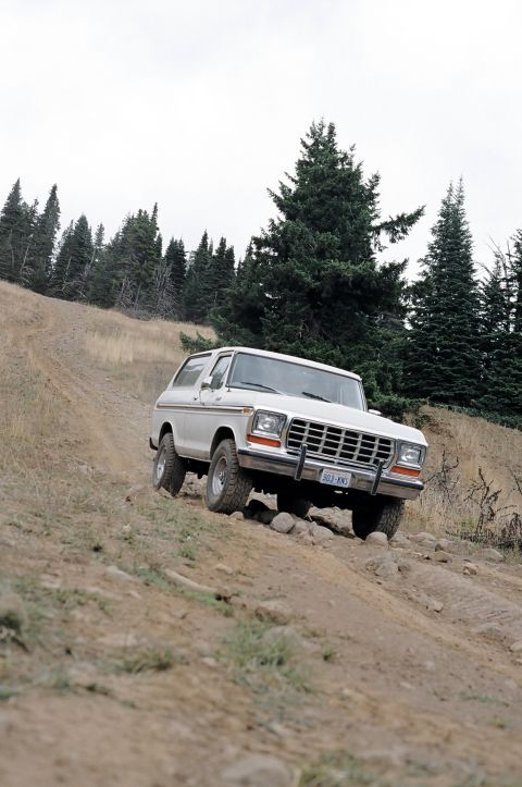 1979 Ford Bronco - This SUV navigates a challenging off-road terrain, with a clear view of its front grille and headlights.