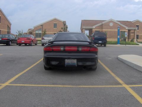 1994 Ford Probe - A black coupe is parked in a lot with other vehicles and buildings in the background.