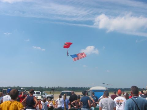 1989 Ford Bronco - A skydiver carrying an American flag descends under a red parachute while a crowd watches below.