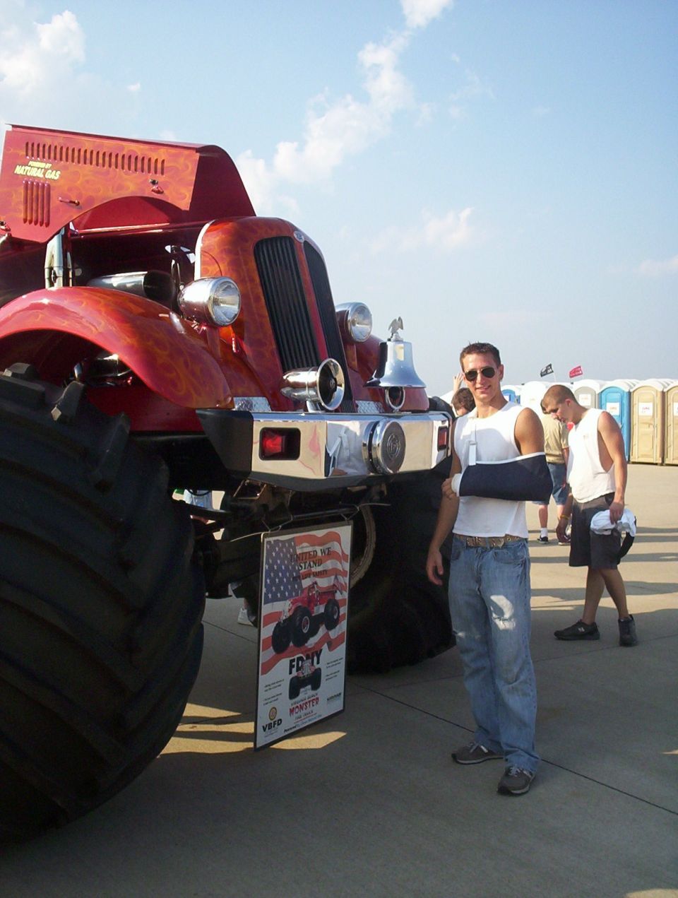 Red monster truck with large tires and a bell, a man with a cast stands nearby