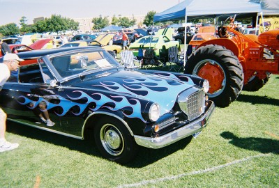 1972 Ford Ranchero - A black car with blue flame decals is parked on grass next to an orange tractor.