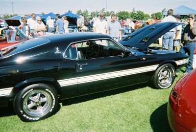 1972 Ford Ranchero - A black 1970 Ford Mustang fastback with white side stripes is displayed at a car show.