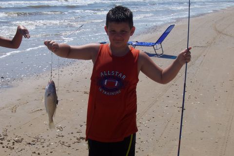 1987 Ford Bronco - A boy proudly displays his catch on a sandy beach, with the ocean waves in the background.