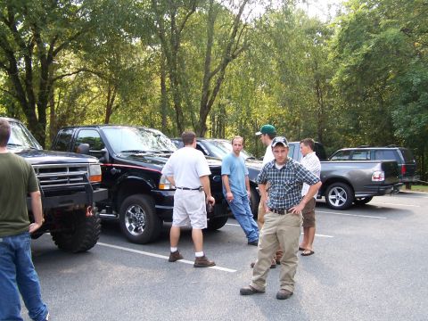 1979 Ford F-150 - A group of men are gathered in a parking lot with several pickup trucks parked nearby.