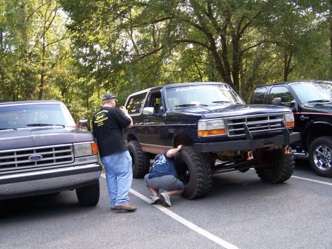 1979 Ford F-150 - Two people inspect a lifted Ford Bronco parked next to other trucks.