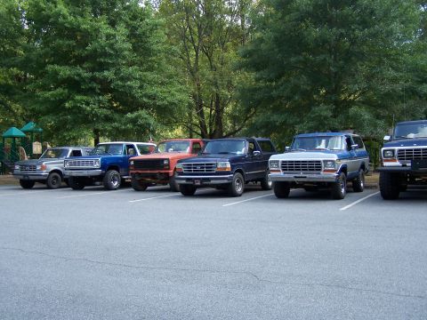 1979 Ford F-150 - A lineup of Ford trucks and SUVs, including a 1979 F-150, parked in a lot with trees in the background.