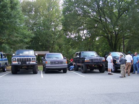 1979 Ford F-150 - Several trucks and SUVs are parked in a lot with trees in the background.