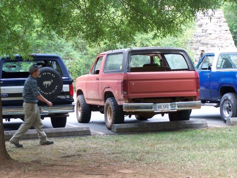 1979 Ford F-150 - A red Ford Bronco with a black top is parked next to other vehicles.