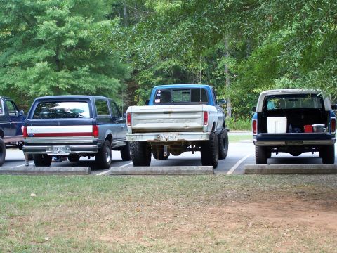 1979 Ford F-150 - Three Ford vehicles, including a pickup and two Broncos, are parked in a lot with trees in the background.