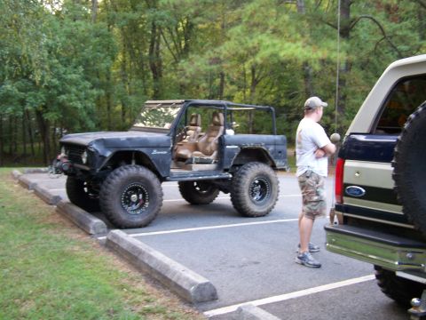 1979 Ford F-150 - A man stands by a lifted black Ford Bronco with its doors off, parked in a lot.