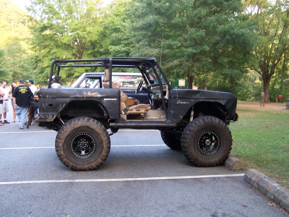 Modified black Ford Bronco with roll cage and large tires parked next to another vehicle
