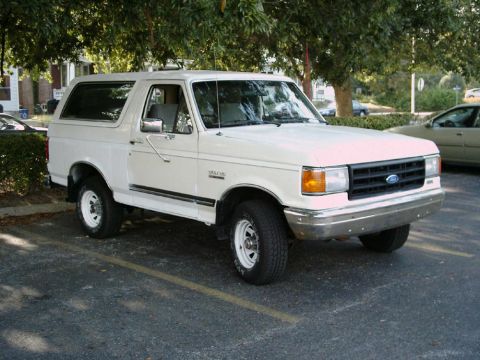1988 Ford Bronco - This white Ford Bronco is parked in a lot, showing its front 3/4 view with chrome bumper and black grille.