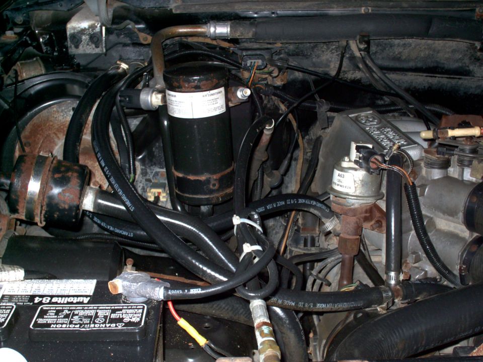 Engine bay of 1988 Ford Bronco with A/C accumulator, heater hoses, distributor, and Autolite battery