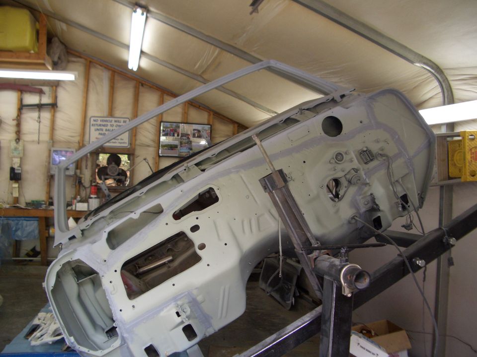 Bare car body shell flipped on rotisserie showing firewall and underbody during restoration