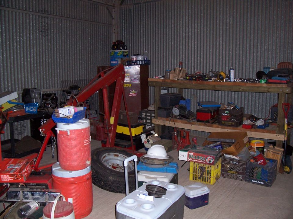 Workshop interior with engine hoist, tool chests, workbench, and various automotive parts and supplies