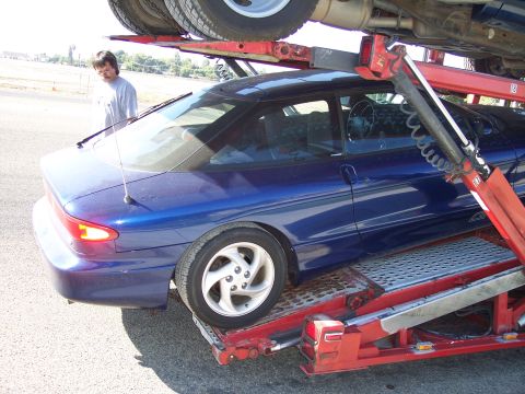 1995 Ford Probe - A blue coupe is being loaded onto a car carrier, with another vehicle above it.