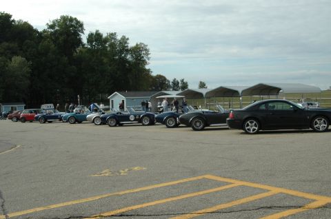 2000 Ford Mustang - A line of classic sports cars and a black 2000 Ford Mustang coupe are parked on asphalt.