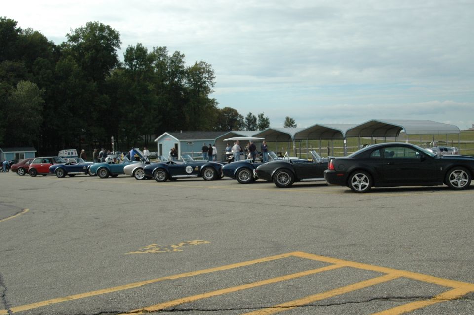 Black 2000 Ford Mustang coupe parked next to several classic Shelby Cobra replicas