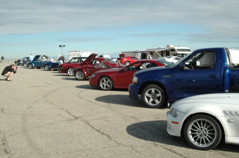 2000 Ford Mustang - A photographer captures a line of vehicles, including Mustangs and a blue pickup truck, on a paved lot.
