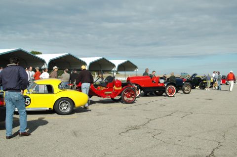 2000 Ford Mustang - Several vintage cars are on display at an outdoor event with spectators milling about.