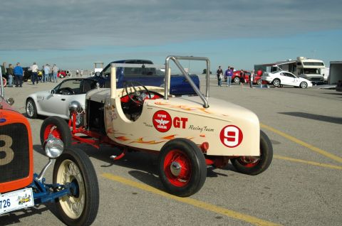 2000 Ford Mustang - A vintage-style custom race car is parked at an outdoor event with other vehicles and people.