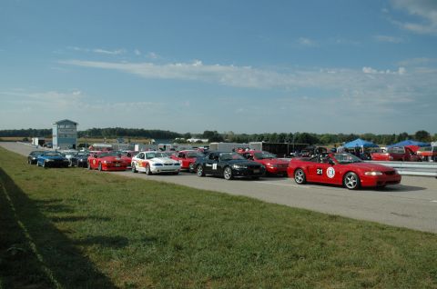 2000 Ford Mustang - Multiple Ford Mustangs are lined up on a racetrack under a partly cloudy sky.