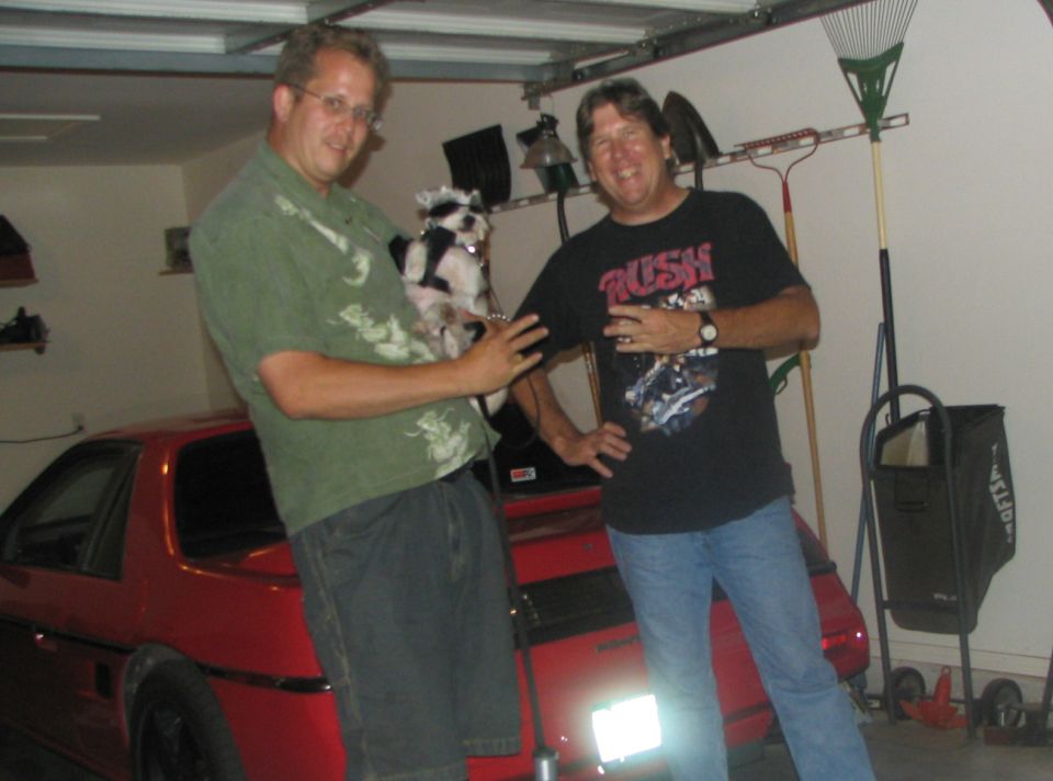 guy holding dog next to red car in garage