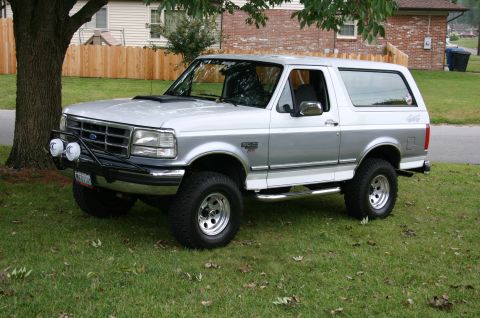 1994 Ford Bronco - This lifted Ford Bronco has a two-tone silver paint job and is parked on a grassy lawn.