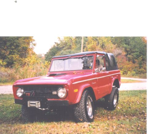 1974 Ford Bronco - A red Ford Bronco is shown from the front three-quarter view, parked outdoors with autumn foliage.